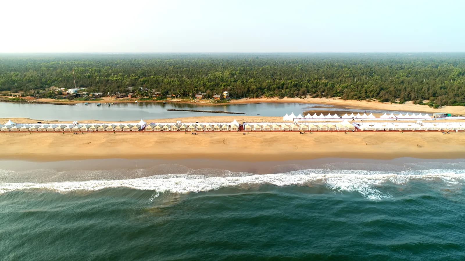 Aerial view of Konark beach in Odisha, featuring golden sandy shores, coastal waves, beachside tents, and lush green forest in the background.