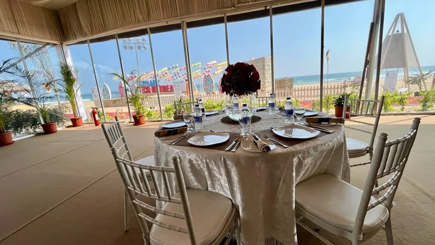 Sunny daytime seafront dining pavilion, table, sea and Konark camp sign at Eco Retreat Konark