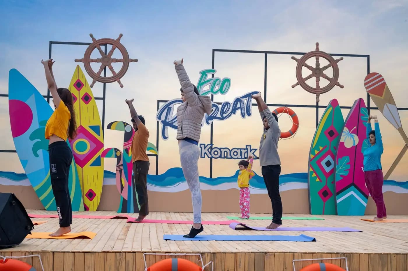 Guests practising yoga on Eco Retreat Konark stage; location sign visible