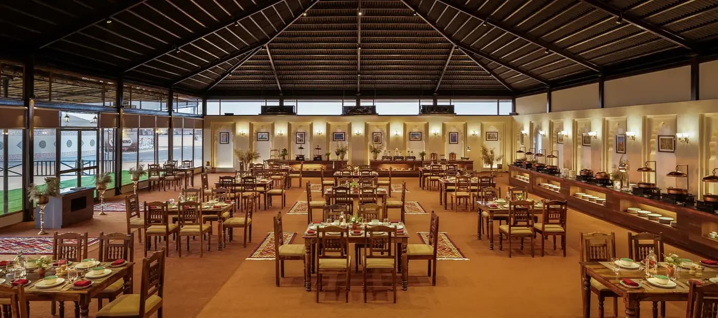 Empty wide dining hall with timber ceiling, tables and buffet line at Rann Utsav — reference